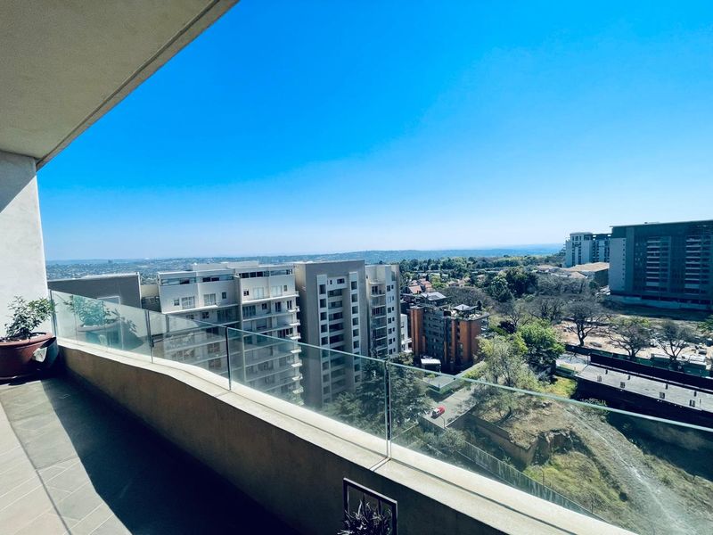 A spacious balcony featuring a modern glass balustrade and tiled flooring, offering expansive elevated views of the surrounding urban landscape.