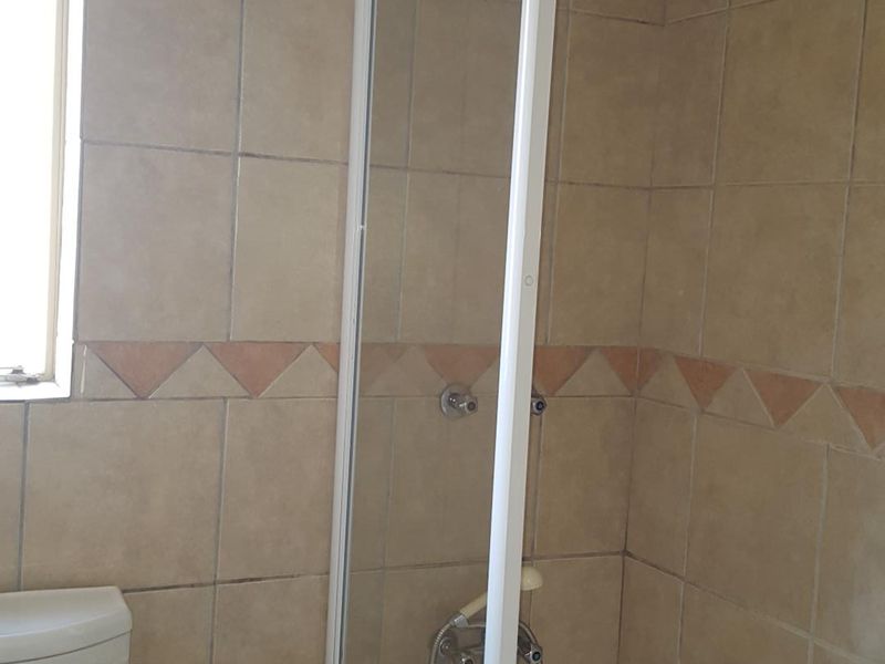 A functional bathroom featuring a bathtub with a glass shower screen, tiled walls, and a standard toilet. The ceiling shows signs of water damage.