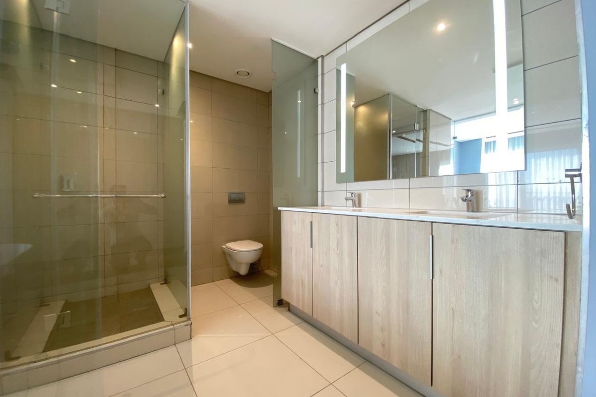 Modern bathroom featuring a double vanity with light wood cabinetry, a frameless glass shower enclosure, and a wall-mounted toilet.