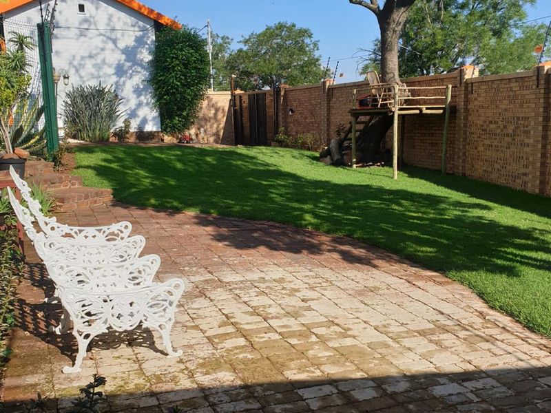 A well-maintained backyard featuring a paved patio area, lush green lawn, and secure brick boundary walls with electric fencing.