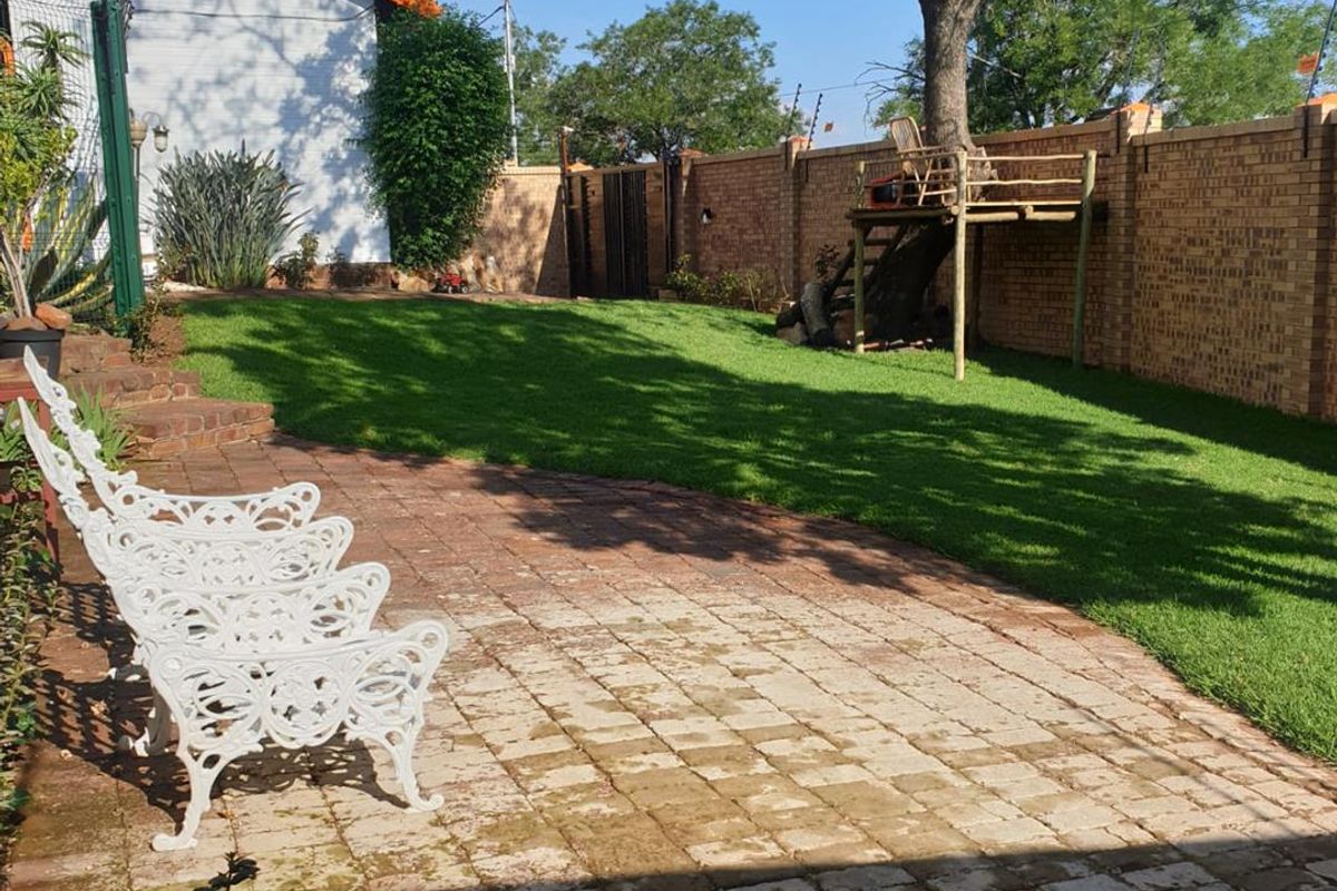 A well-maintained backyard featuring a paved patio area, lush green lawn, and secure brick boundary walls with electric fencing.