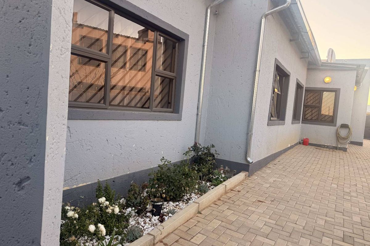 A well-maintained rear exterior view featuring paved walkways, a raised garden bed, and modern aluminium window frames along the side of the house.