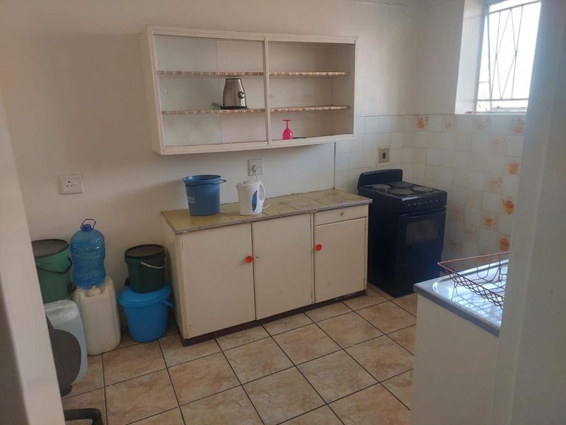 A functional kitchen featuring tiled flooring, built-in cabinetry, and a tiled splashback, offering potential for modernization and cosmetic updates.