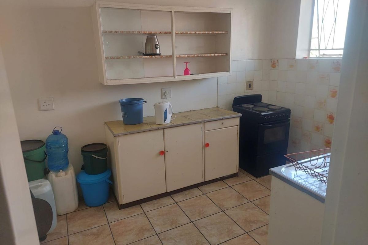 A functional kitchen featuring tiled flooring, built-in cabinetry, and a tiled splashback, offering potential for modernization and cosmetic updates.
