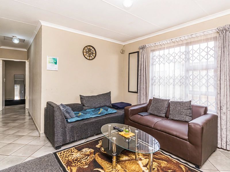 A functional living room featuring tiled flooring, neutral wall tones, and a large window fitted with a security gate.