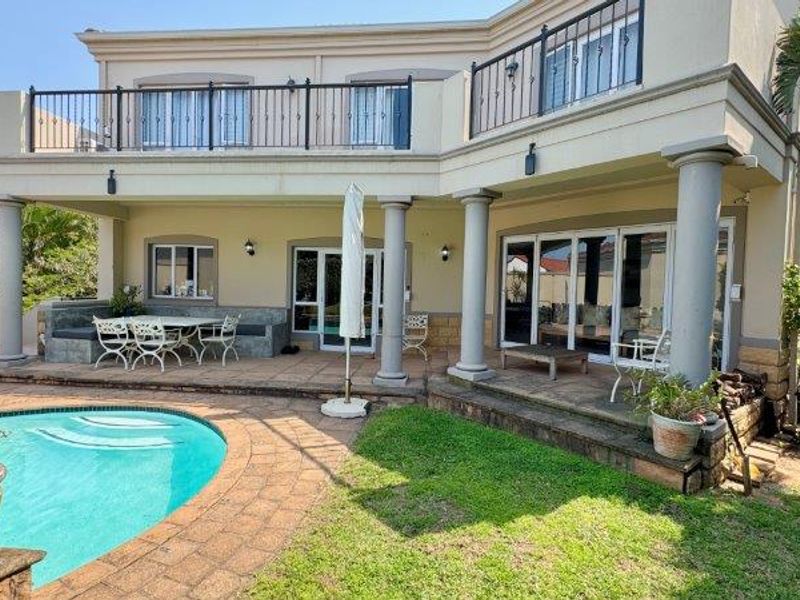 Rear exterior view of the townhouse featuring a swimming pool, paved patio area, and an upper-level balcony with metal railings.