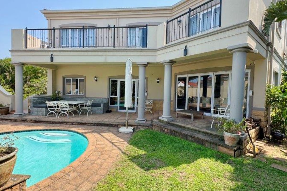 Rear exterior view of the townhouse featuring a swimming pool, paved patio area, and an upper-level balcony with metal railings.