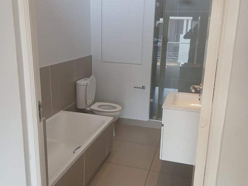 A clean, modern bathroom featuring a bathtub, separate shower enclosure, wall-mounted vanity, and neutral floor-to-ceiling tiling.