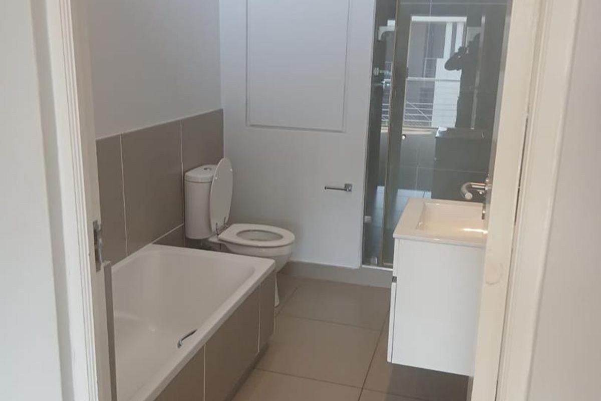 A clean, modern bathroom featuring a bathtub, separate shower enclosure, wall-mounted vanity, and neutral floor-to-ceiling tiling.