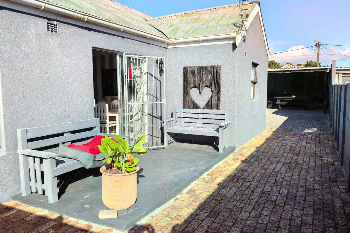 A paved rear patio area featuring a grey painted concrete surface, security gate access to the interior, and a brick-paved side walkway.