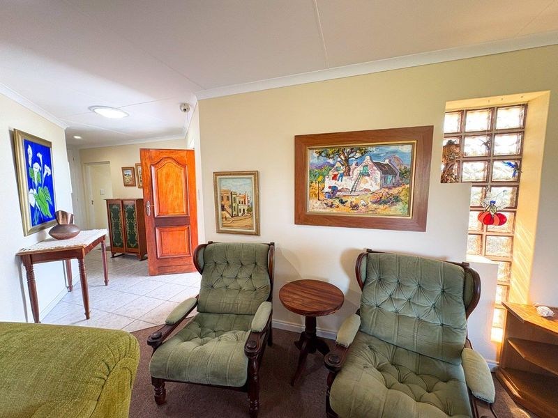 A living area featuring a glass block feature wall, tiled and carpeted flooring, and recessed ceiling lighting, leading into an adjacent hallway.