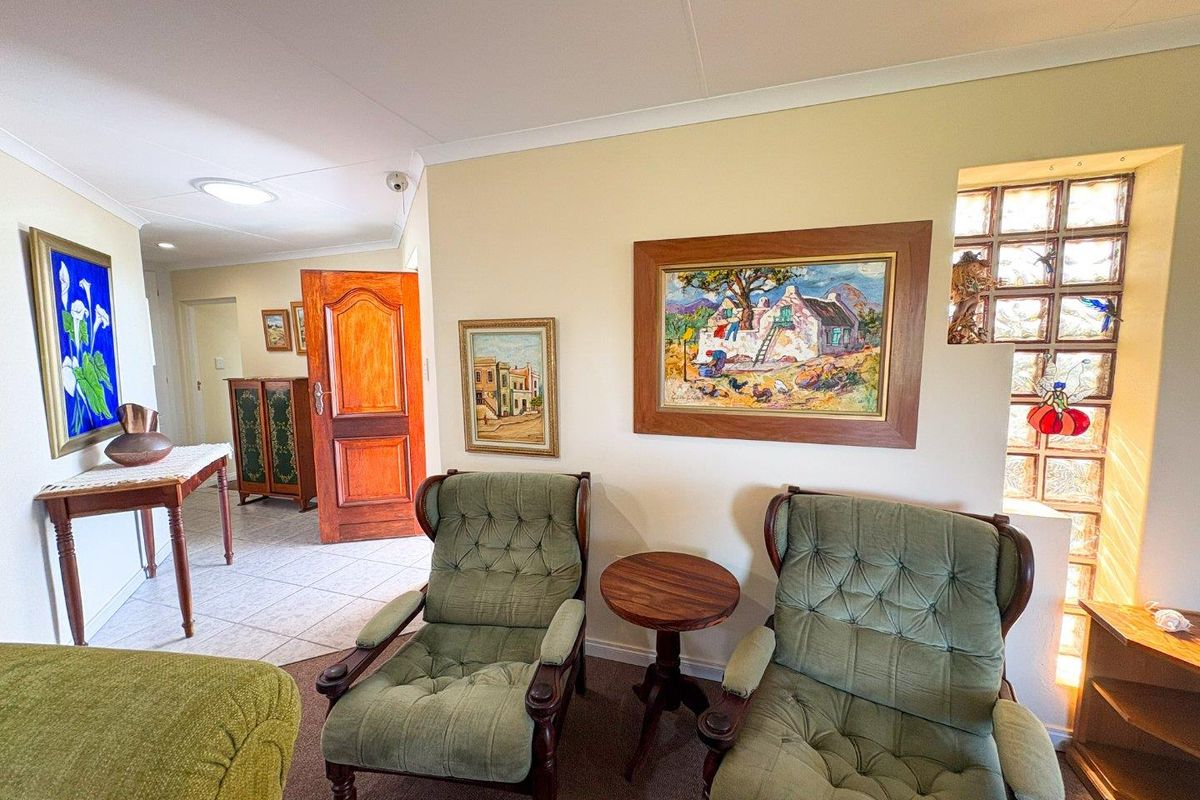 A living area featuring a glass block feature wall, tiled and carpeted flooring, and recessed ceiling lighting, leading into an adjacent hallway.