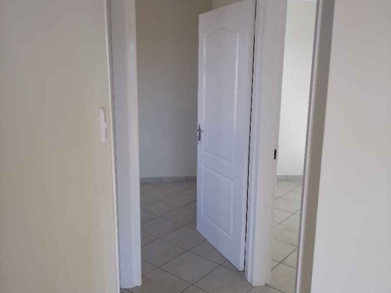 A clean, neutral hallway featuring tiled flooring and white internal doors, providing access to adjacent rooms.