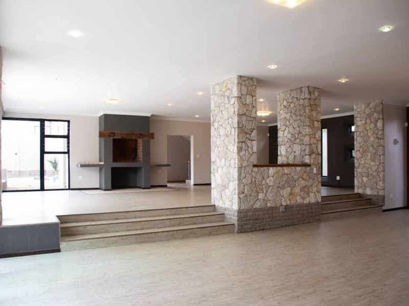 Spacious open-plan living area featuring striking stone-clad pillars, a built-in fireplace with a timber mantel, and multi-level flooring with recessed lighting.