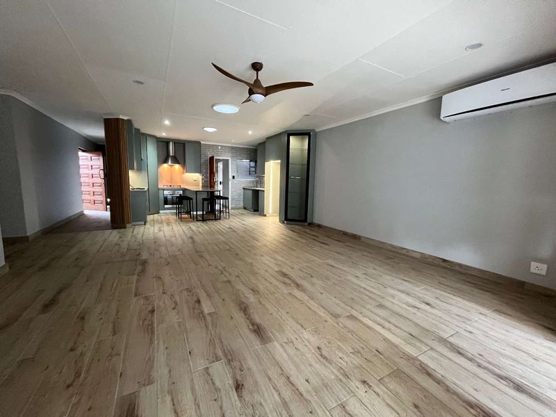 Spacious open-plan living and kitchen area featuring modern wood-look tile flooring, built-in cabinetry, integrated appliances, and climate control.