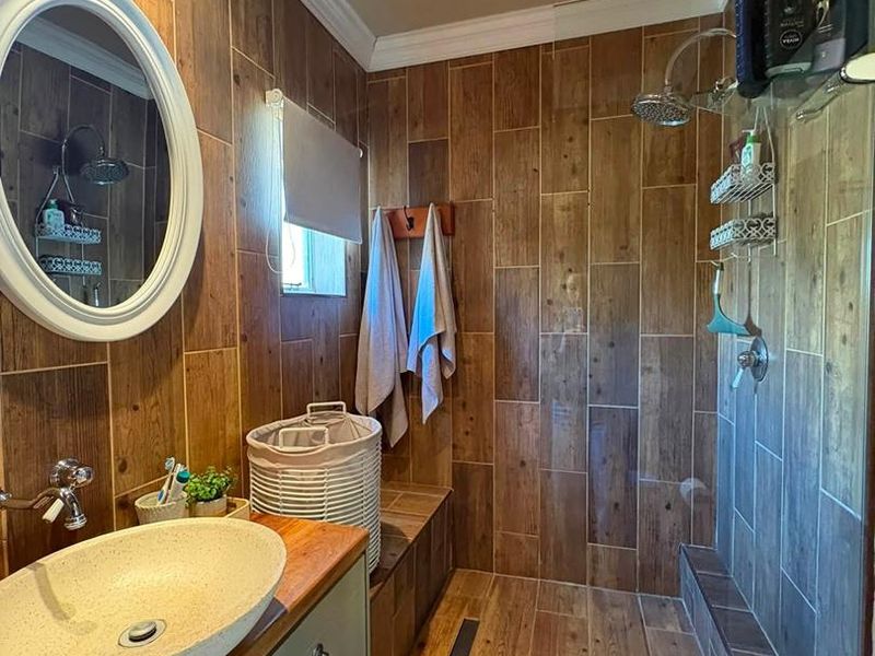 Modern bathroom featuring wood-look tile wall cladding, a vessel sink on a vanity cabinet, and a spacious walk-in shower with a rain shower head.