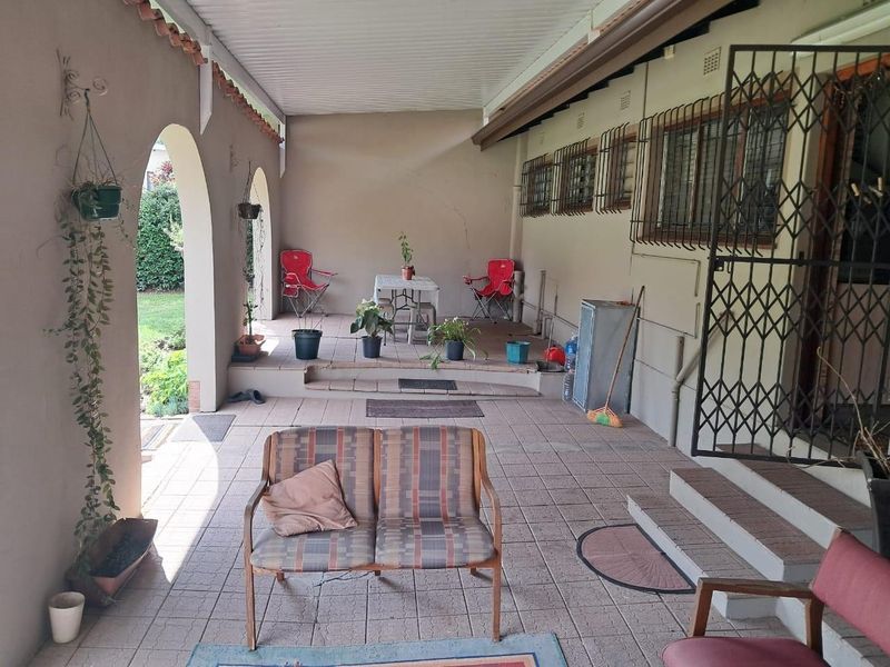 A covered outdoor patio area featuring tiled flooring, arched architectural details, and security features on windows and doors.