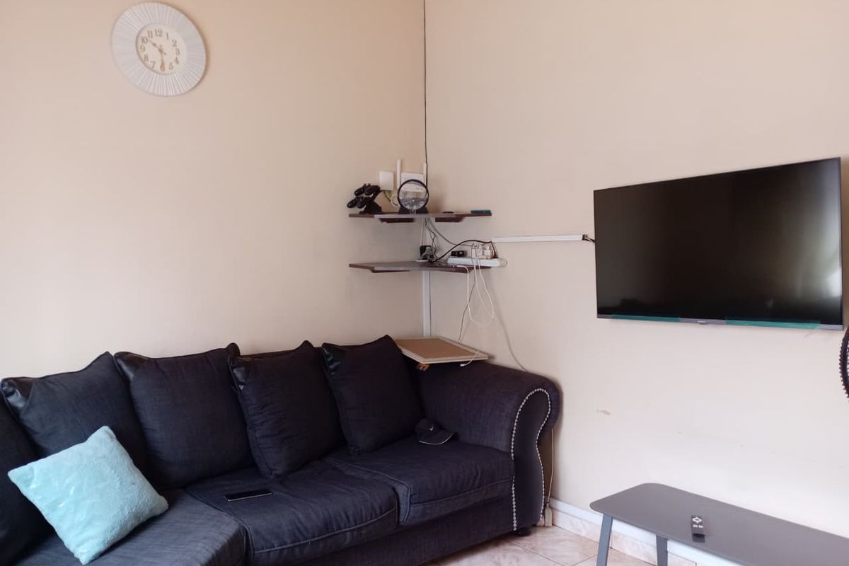 A living room area featuring tiled flooring and a wall-mounted television setup with corner shelving.
