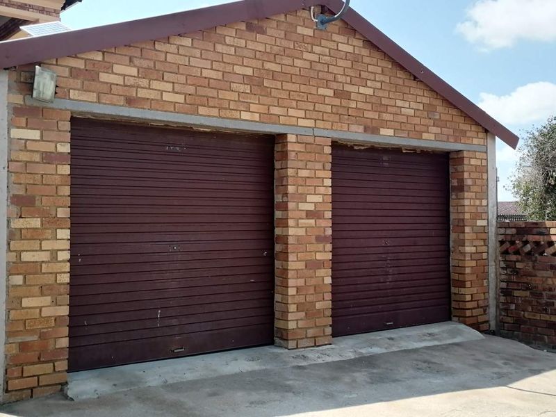 A detached double garage featuring face brick construction and two roller doors, set on a concrete driveway with an adjacent brick boundary wall.