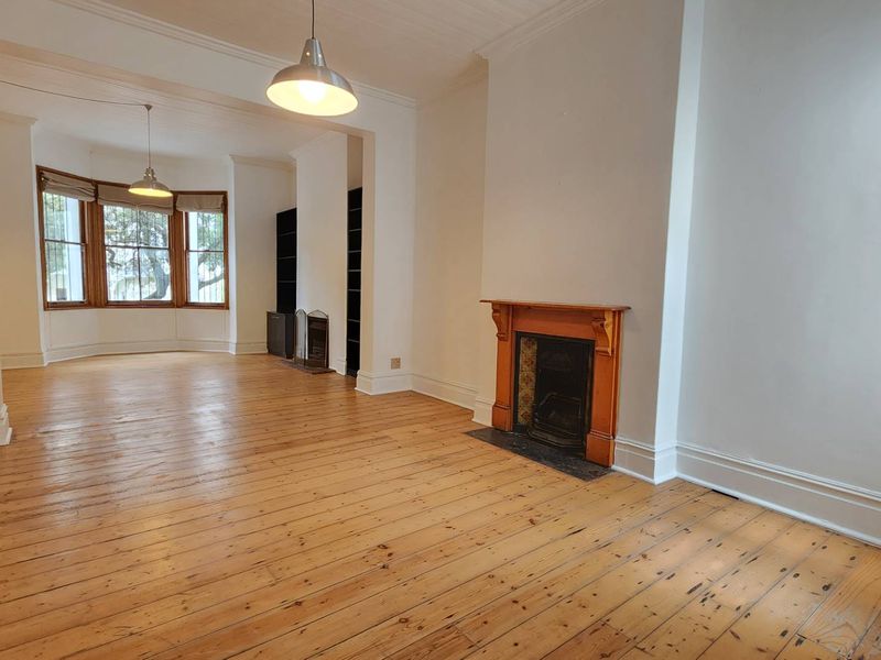 Spacious living area featuring original timber flooring, a classic fireplace with a timber mantel, and a bright bay window.