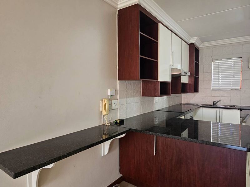 A functional kitchen featuring dark granite countertops, ample built-in cabinetry, a breakfast bar, and a tiled backsplash, offering a clean and practical workspace.