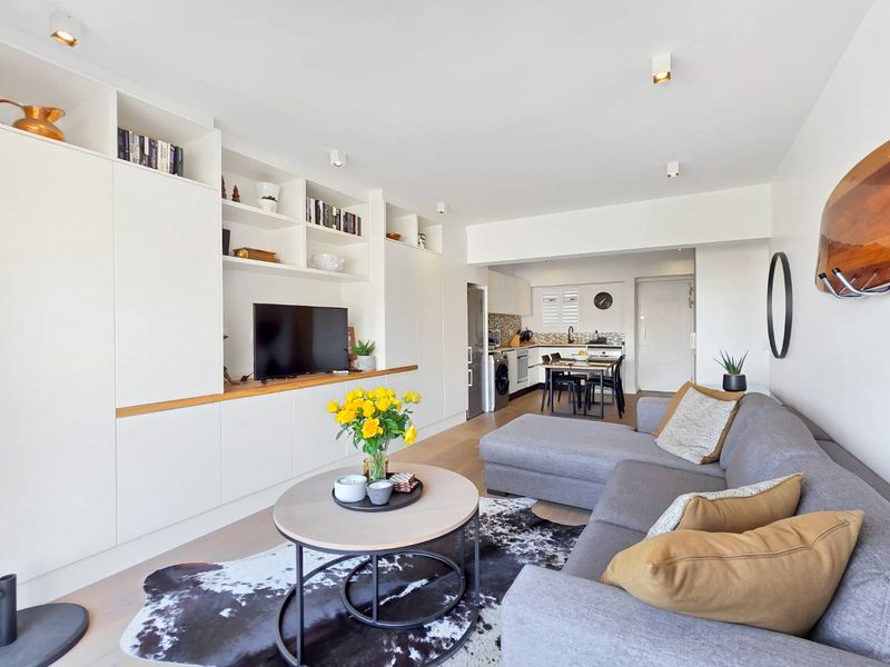A bright open-plan living and kitchen area featuring modern built-in cabinetry, hardwood flooring, and recessed lighting, creating a seamless and functional living space.