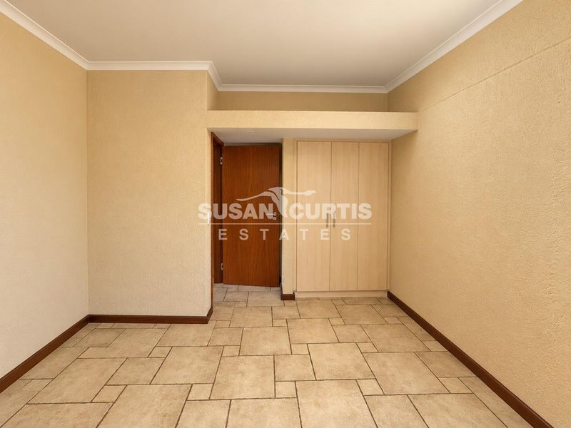 An empty bedroom featuring neutral tiled flooring, coved cornicing, and built-in wooden cupboards.
