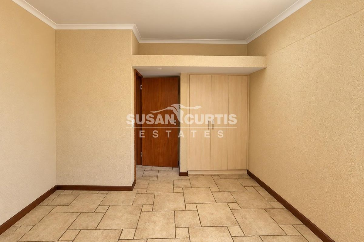 An empty bedroom featuring neutral tiled flooring, coved cornicing, and built-in wooden cupboards.