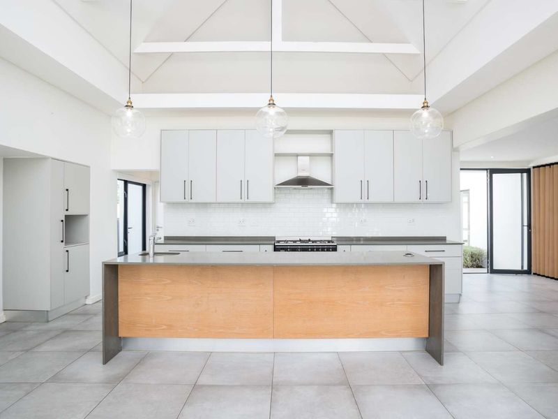 Modern, spacious kitchen featuring a large central island, stone countertops, subway tile backsplash, and high vaulted ceilings with exposed beams.