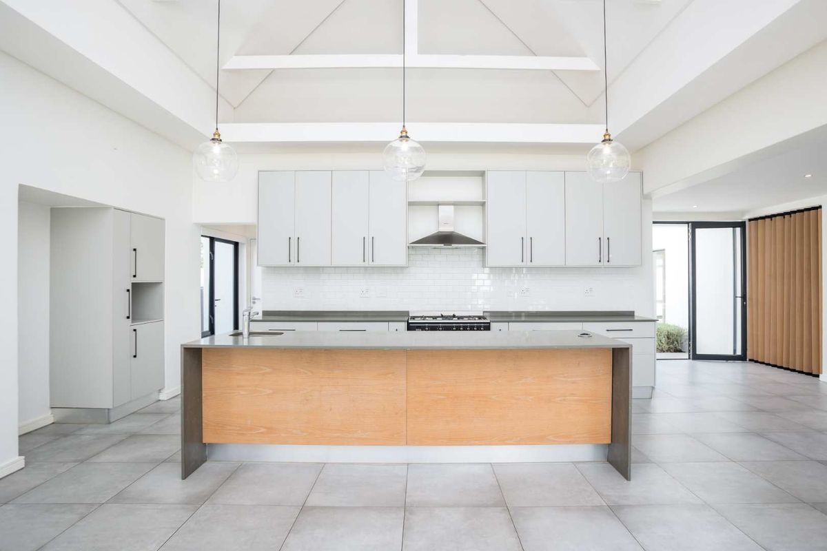 Modern, spacious kitchen featuring a large central island, stone countertops, subway tile backsplash, and high vaulted ceilings with exposed beams.