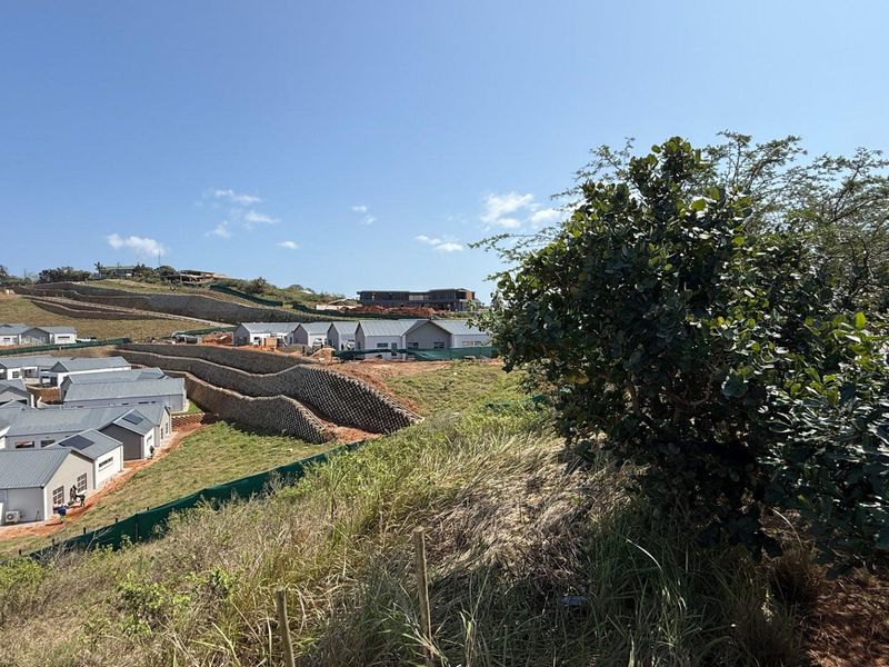 An elevated view of a residential development site featuring multiple houses, retaining walls, and sloped landscape under a clear blue sky.