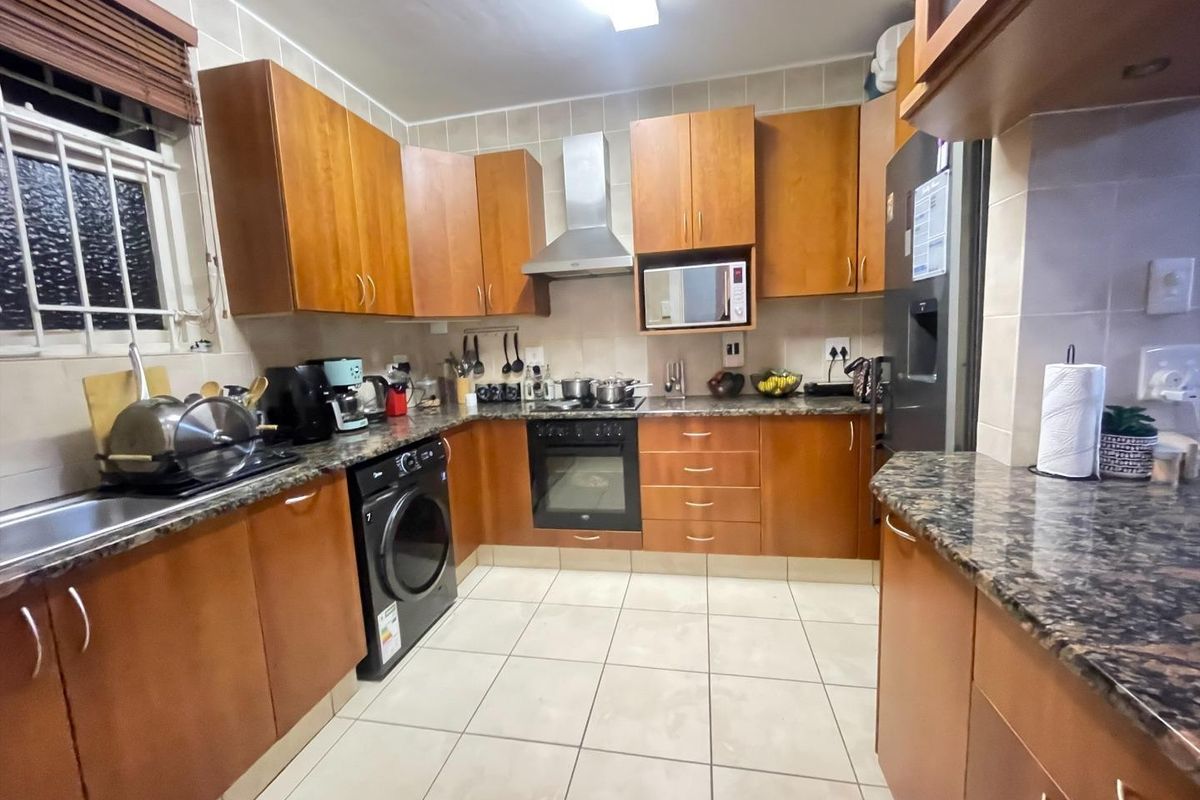 A functional kitchen featuring warm-toned wooden cabinetry, granite countertops, a tiled backsplash, and integrated stainless steel appliances including an oven and extractor fan.