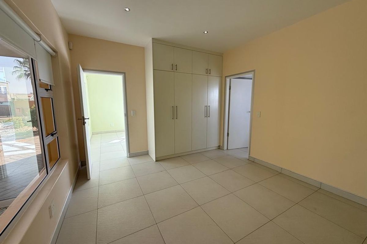 A bright, empty bedroom featuring neutral tiled flooring, built-in floor-to-ceiling cabinetry, and recessed ceiling lighting.