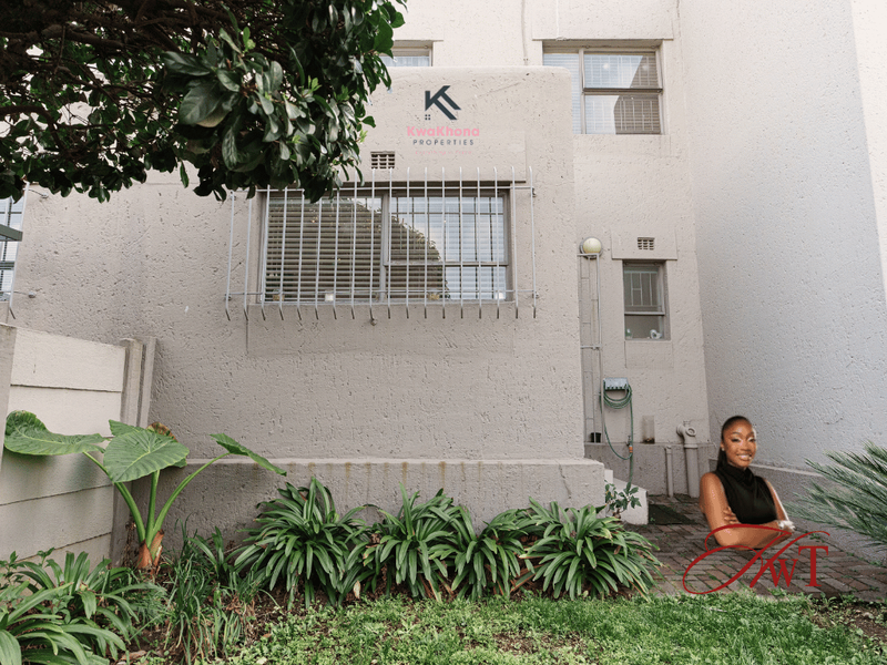 Rear exterior view of the townhouse featuring a paved patio area, security bars on windows, and established garden beds against the boundary wall.