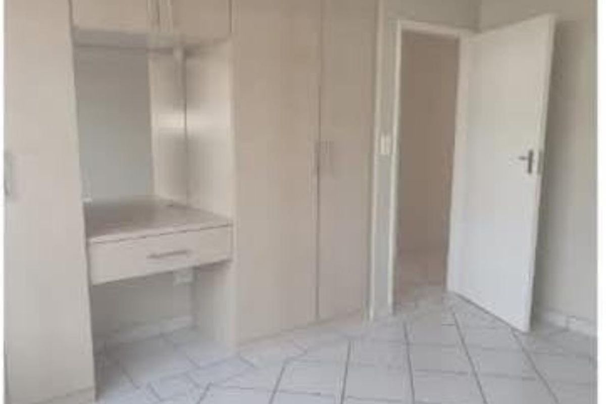 A bedroom featuring built-in cupboards with an integrated vanity desk and neutral tiled flooring.