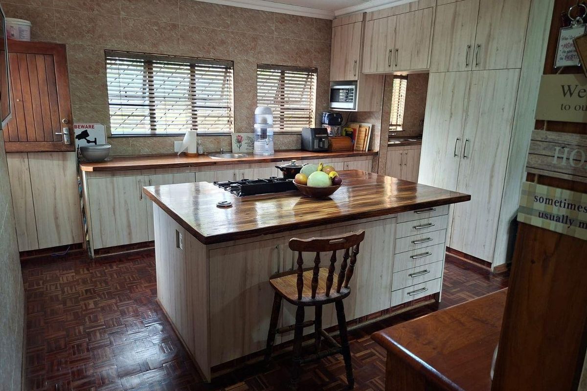 Spacious kitchen featuring a central island with a built-in gas hob, light wood cabinetry, and a separate scullery area with ample storage.