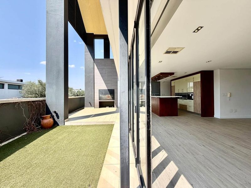 Modern open-plan living area featuring a sleek kitchen with island, flowing seamlessly onto a spacious covered patio with a built-in fireplace.