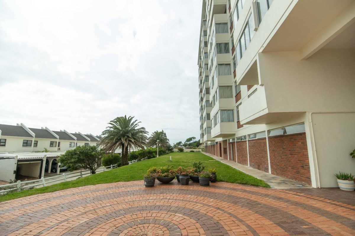 A view of the rear exterior of a multi-story apartment building featuring a paved patio area and a well-maintained lawn.