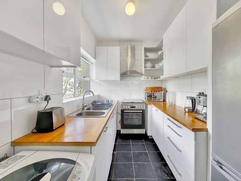 A compact, well-maintained kitchen featuring white cabinetry, wooden countertops, stainless steel appliances, and tiled finishes.