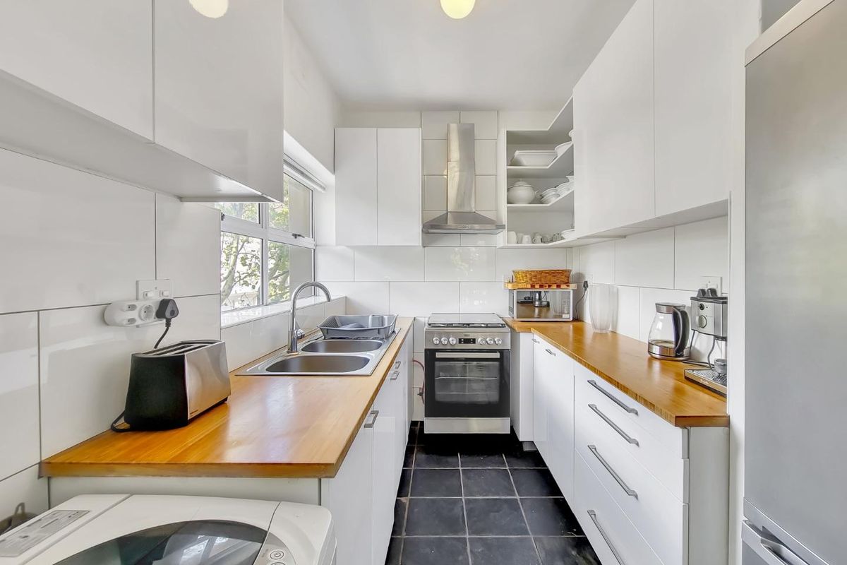 A compact, well-maintained kitchen featuring white cabinetry, wooden countertops, stainless steel appliances, and tiled finishes.