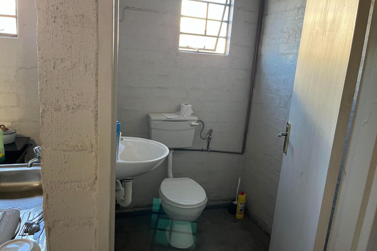 A functional bathroom featuring a standard toilet and wall-mounted basin, characterized by exposed brick walls and concrete flooring.