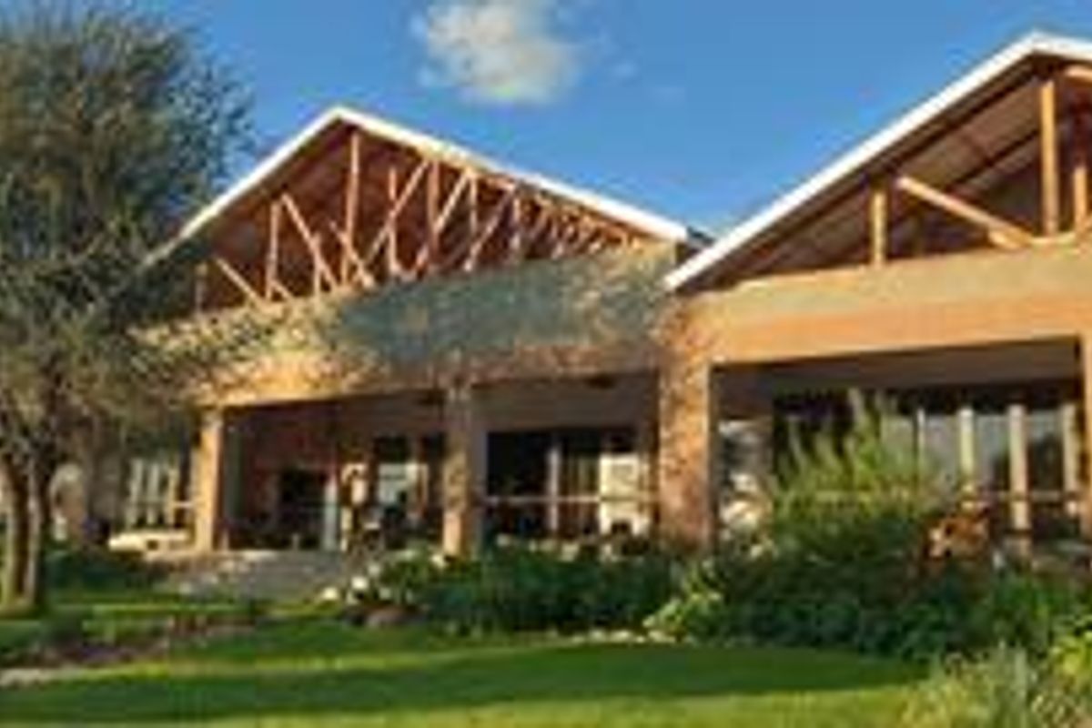 Rear view of a large house featuring exposed timber roof trusses, brick facade, and a spacious covered patio overlooking a landscaped garden.