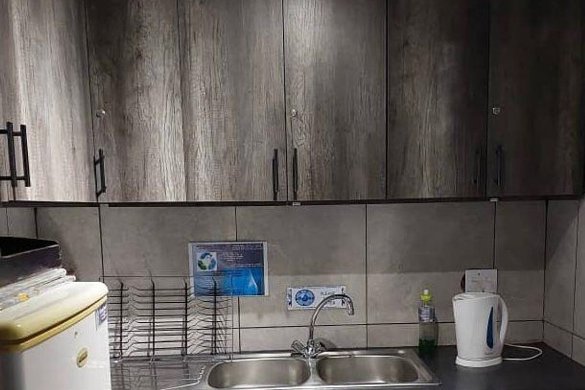 A compact kitchenette featuring wood-look cabinetry, a double-basin stainless steel sink, and tiled splashback, suitable for office or utility use.