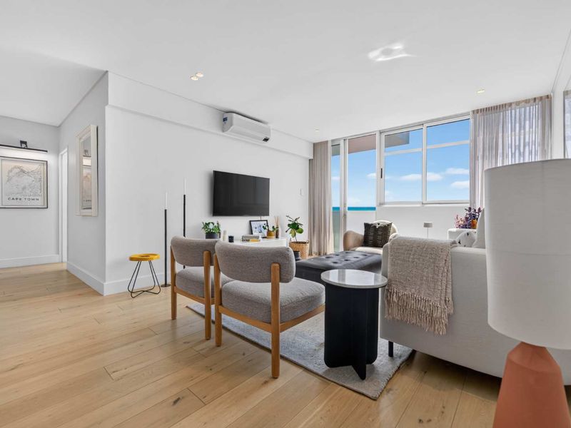 Bright and modern living room featuring light timber flooring, recessed lighting, a wall-mounted air conditioning unit, and large sliding doors leading to a balcony.