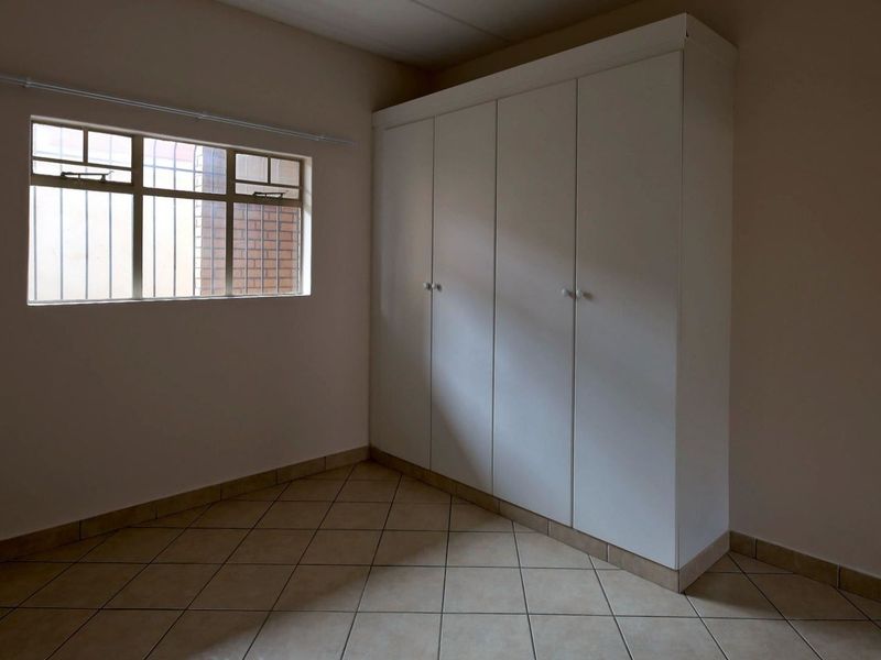 An empty bedroom featuring tiled flooring and a built-in wardrobe with white cabinetry.