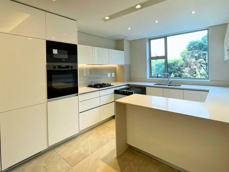 Modern, well-appointed kitchen featuring high-gloss cabinetry, stone countertops, integrated appliances, and a functional U-shaped layout with ample natural light.