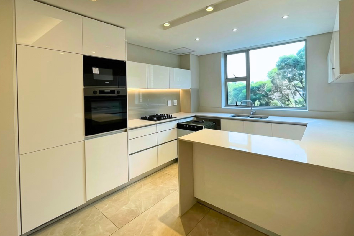 Modern, well-appointed kitchen featuring high-gloss cabinetry, stone countertops, integrated appliances, and a functional U-shaped layout with ample natural light.