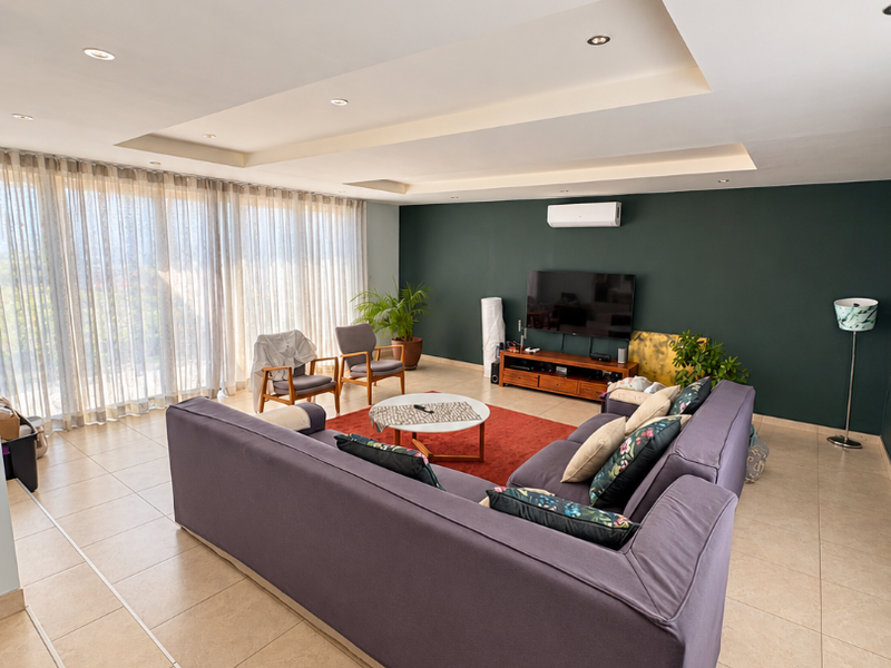 Spacious living room featuring a modern tray ceiling with recessed lighting, tiled floors, and a large window wall with floor-to-ceiling curtains.