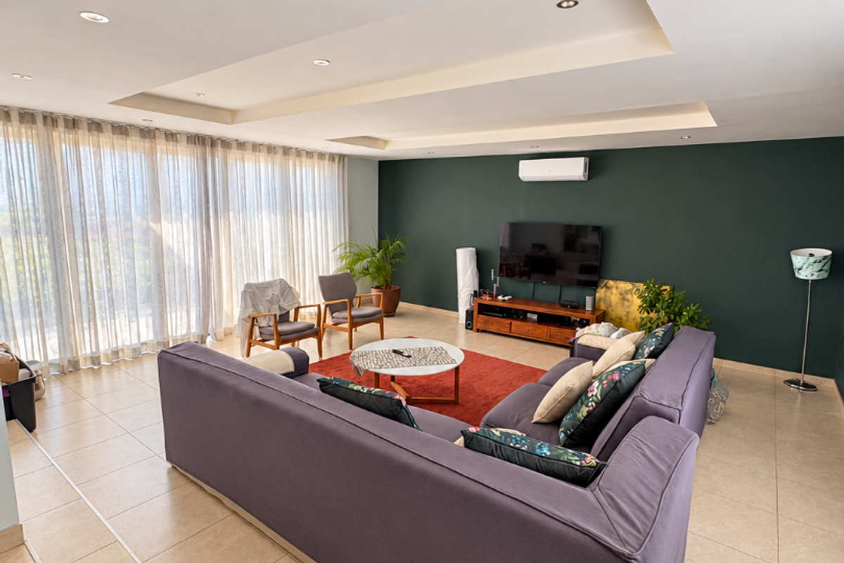 Spacious living room featuring a modern tray ceiling with recessed lighting, tiled floors, and a large window wall with floor-to-ceiling curtains.