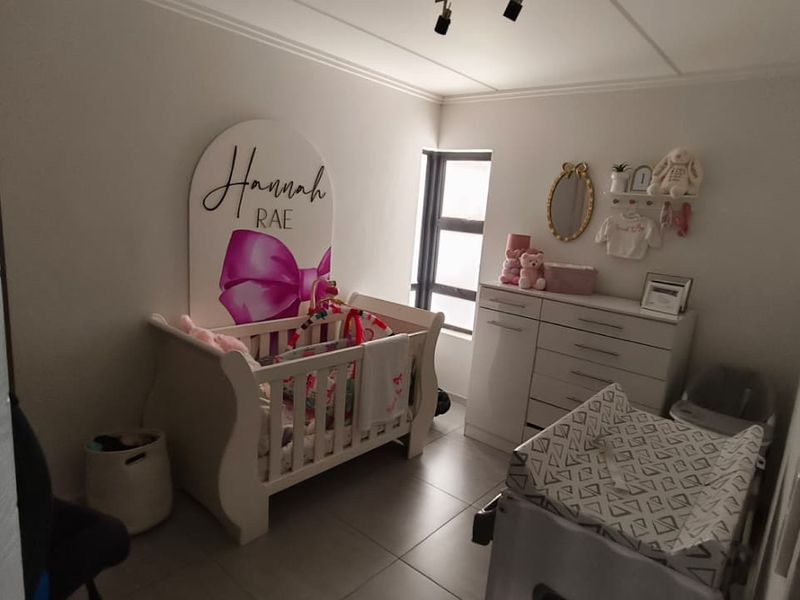 A functional bedroom featuring tiled flooring and an aluminium window frame, currently utilized as a nursery.
